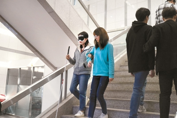 시각장애 체험 중인 도우미 학생이 안내인에 의지해 천천히 계단을 내려가고 있다.